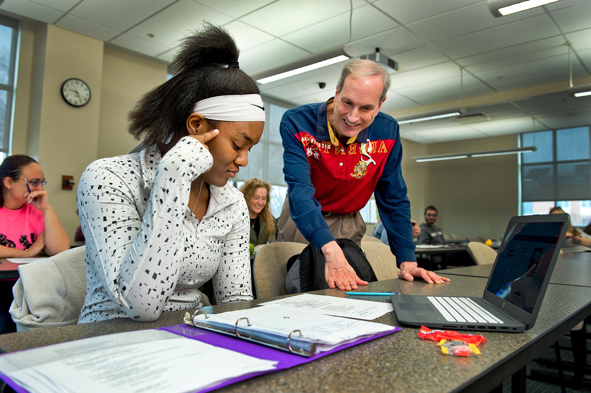 A male professor teaching a female student with a notebook and laptop Spanish